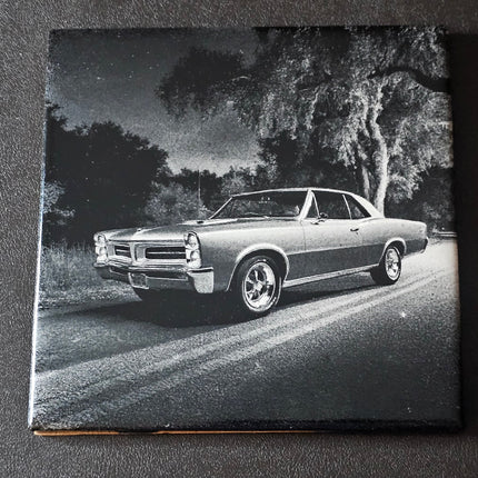 Black and white photo of a classic 65 GTO on a road with trees in the background