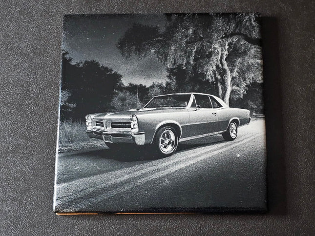 Black and white photo of a classic 65 GTO on a road with trees in the background