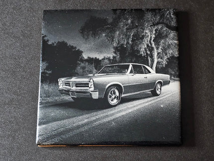 Black and white photo of a classic 65 GTO on a road with trees in the background