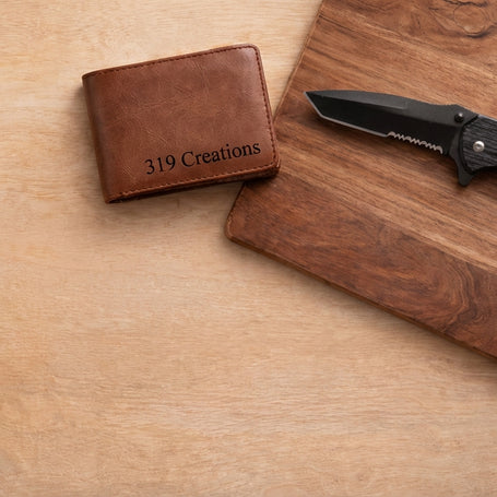Brown leather wallet and black folding knife on a wooden surface with '319 Creations' branding.